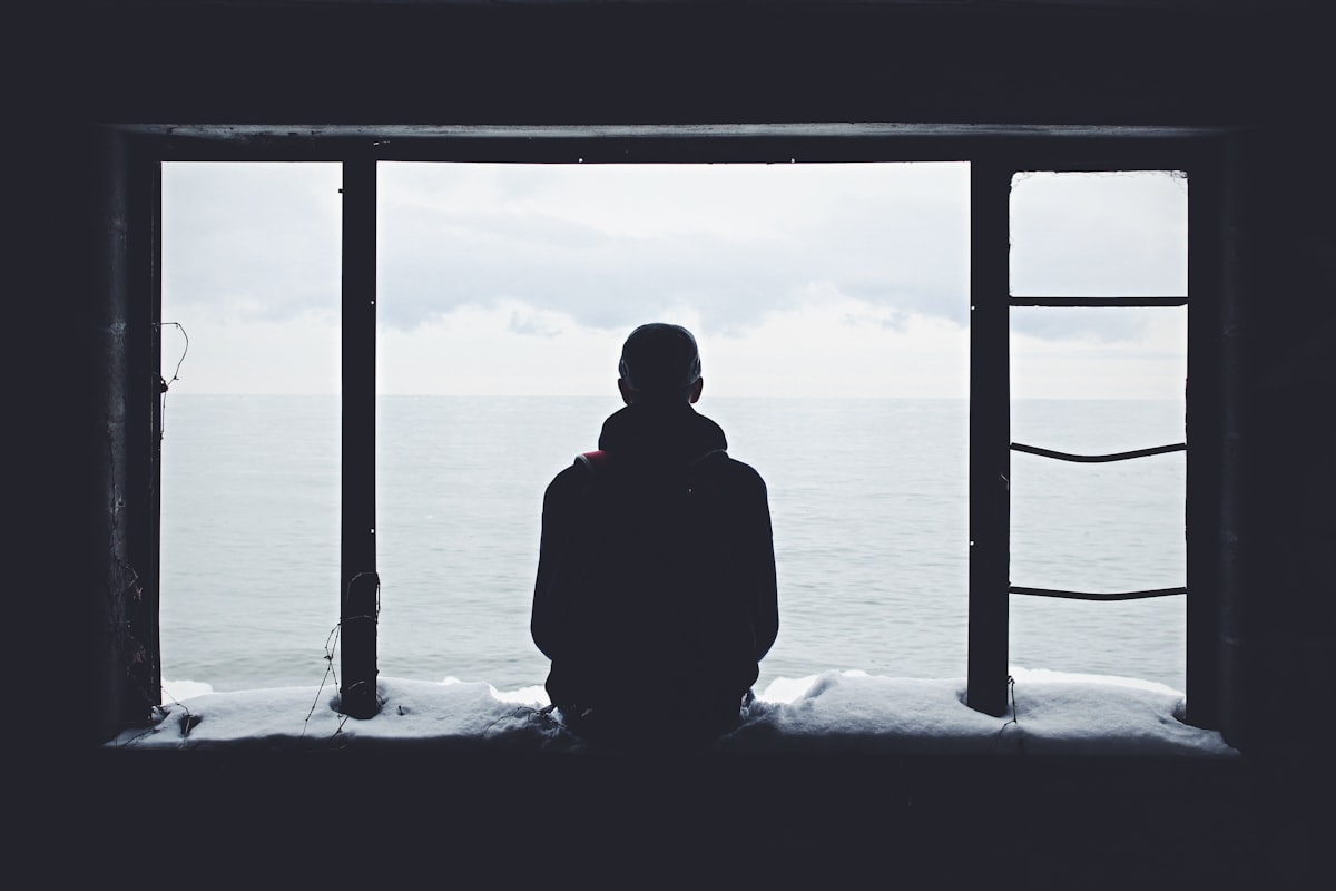 Silhouette of a person looking out through a window at the sea